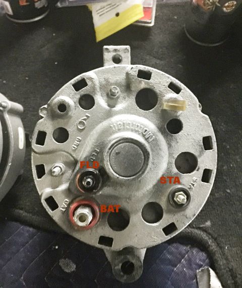 1978 Ford Bronco - The rear view of a silver alternator with labeled terminals BAT, FLD, and STA. The alternator is mounted on a dark surface, possibly a work…