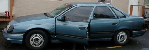 1986 Ford Taurus - The 1986 Ford Taurus sedan is shown from the side with the front passenger door ajar.
