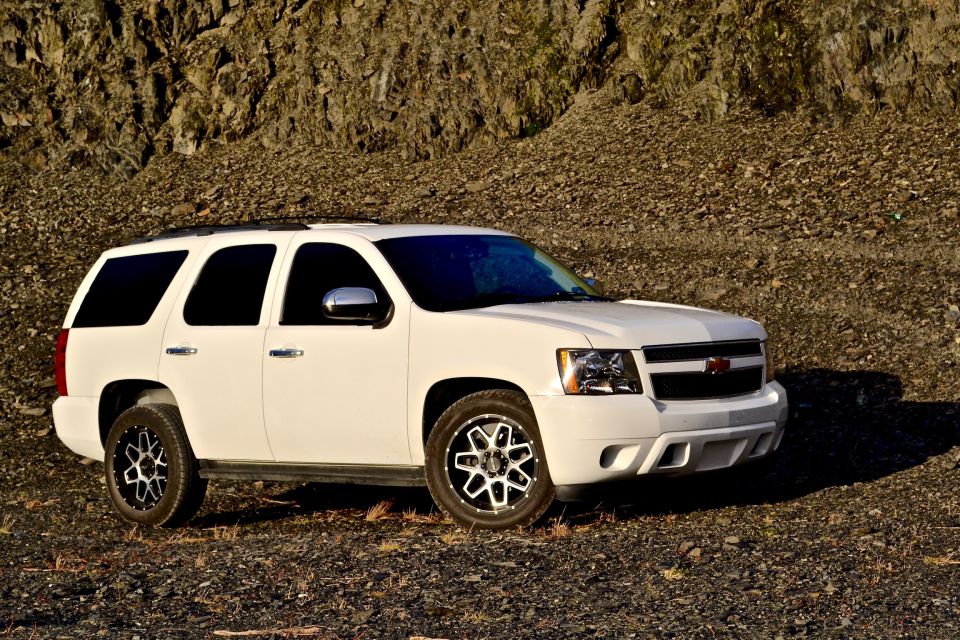White Chevrolet Tahoe SUV with custom wheels parked on gravel.