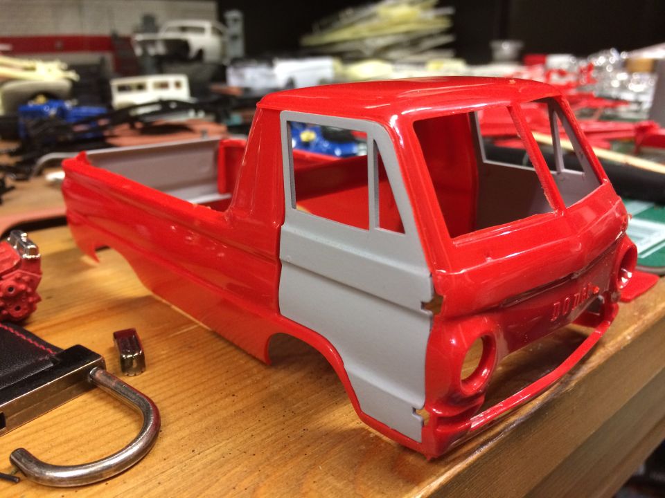Red and gray model pickup truck body on a workbench with model parts.
