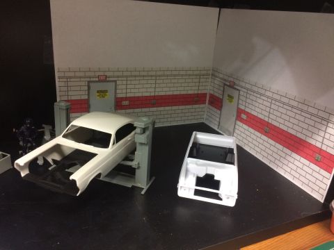 1989 Ford Bronco - A white 1989 Ford Bronco body is staged in a diorama garage setting with a car lift and another vehicle body in the foreground. A small fig…