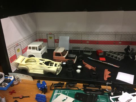 1989 Ford Bronco - A model car garage scene with various unassembled car parts and two partially built model car bodies. A white pickup truck body and a tan p…