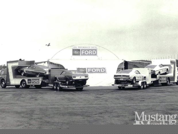 Two Ford car haulers each carrying two Ford Mustangs, parked in front of a Ford branded tent.