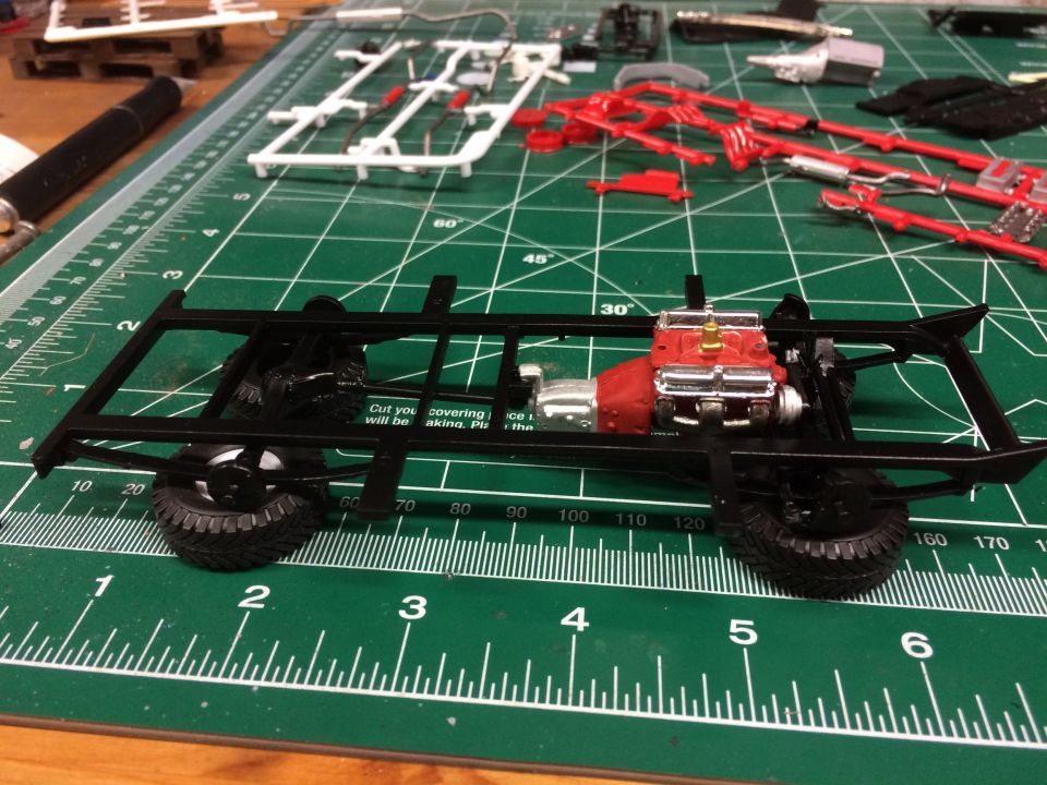 Model car chassis with red engine on a green cutting mat with model parts.
