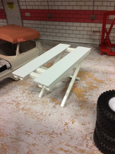1989 Ford Bronco - A white workbench with two slatted surfaces is shown in the foreground, set against a backdrop of a brick wall with red accents. A portion…
