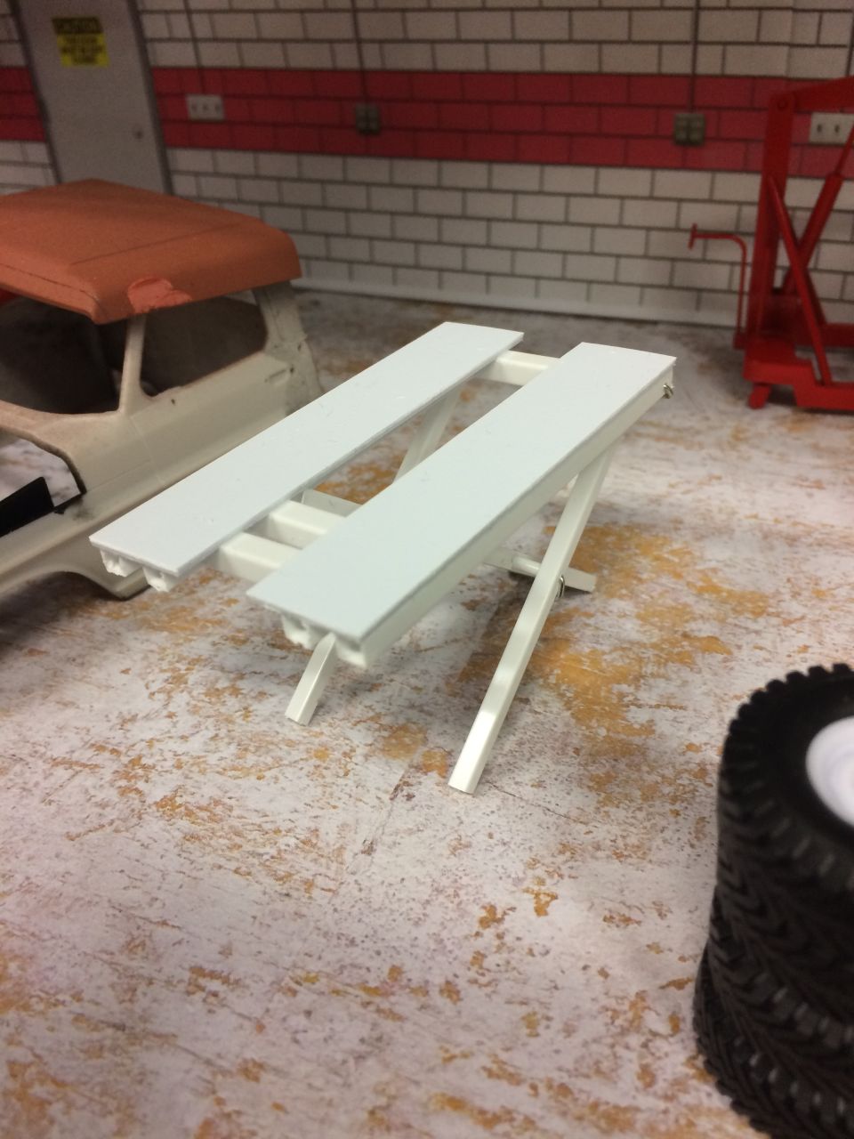 White slatted workbench in a garage setting with a vehicle part and tire.