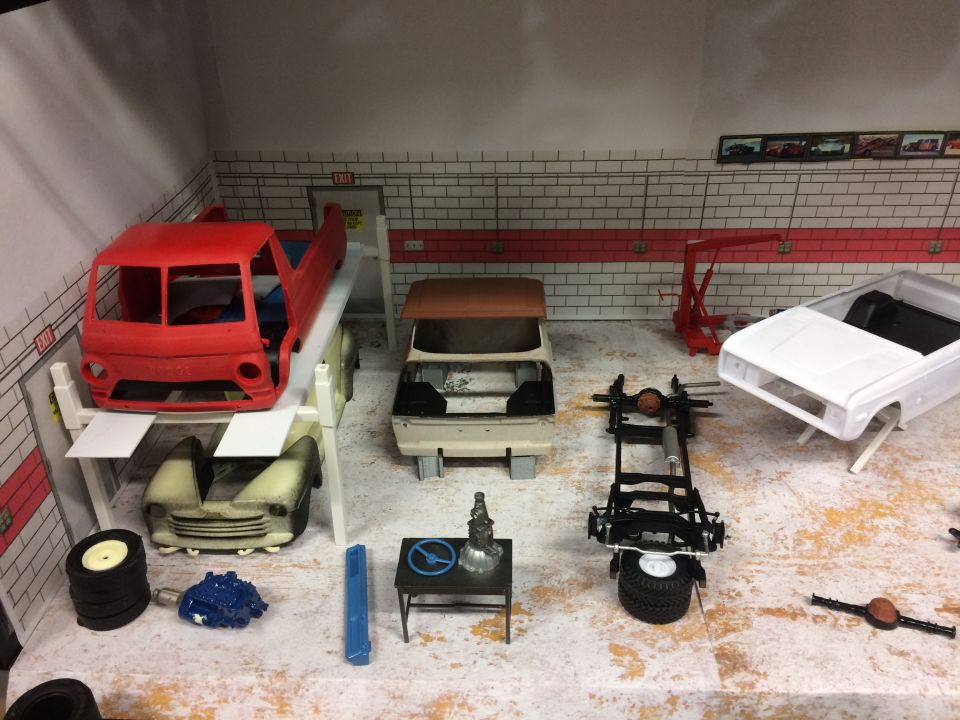 Miniature garage scene with unfinished model cars and parts.