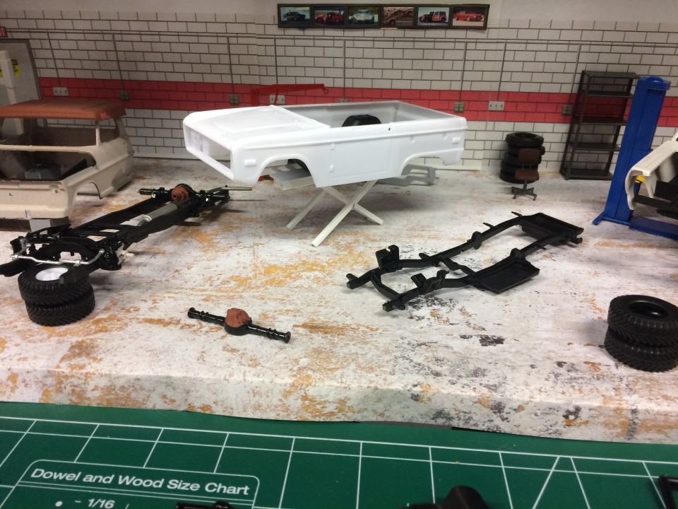 Model Ford Bronco body and chassis with parts in a garage diorama.