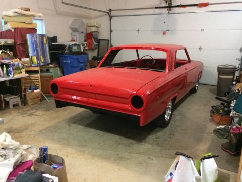 1964 Ford Fairlane - A bright red, two-door coupe is parked in a garage. The car appears to be undergoing restoration, with its interior gutted and the body fre…