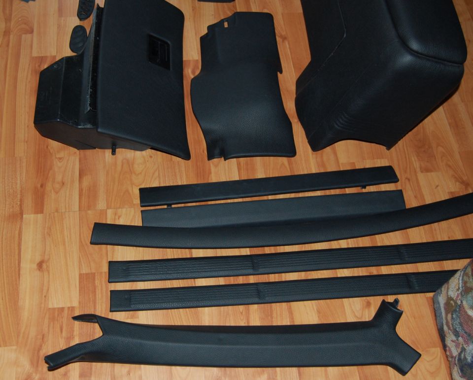 Set of black interior trim panels and door sill plates laid out on a wood floor