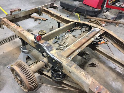 1984 Ford Bronco - The rusty frame of a vintage truck or SUV is shown on jack stands in a garage. Modifications appear to be underway, with new brackets welde…