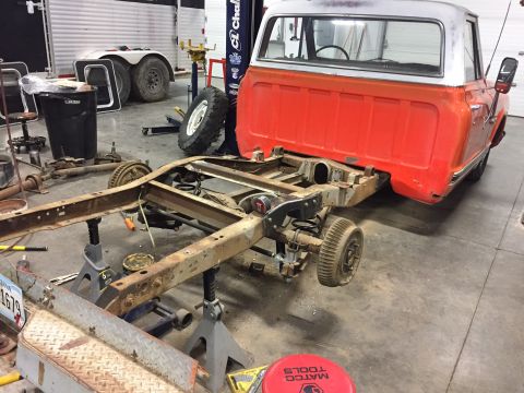 1984 Ford Bronco - The rear half of a vintage orange and white pickup truck is shown disassembled and supported by jack stands in a garage. The frame, suspens…
