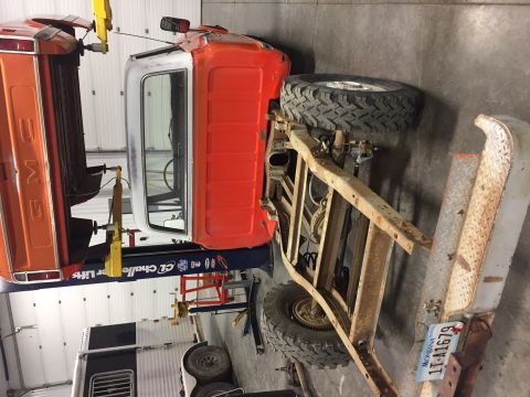 1984 Ford Bronco - The chassis and cab of an orange and white pickup truck are elevated on a lift. A large off-road tire is mounted on the rear axle of the ch…