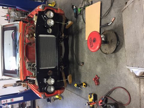 1984 Ford Bronco - The front end of an orange and white vehicle, likely a truck or SUV, is disassembled on a lift in a garage. The radiator, headlights, and f…