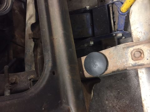 1984 Ford Bronco - A black rubber plug with the text "cpp" embossed on it is installed in a rusty metal bracket. A yellow jack is visible in the background.