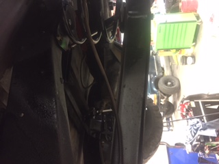 1984 Ford Bronco - The underside of a vehicle showing the frame, exhaust system, and suspension components. A green tool chest and other shop equipment are vi…