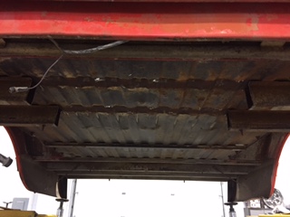 1984 Ford Bronco - The underside of a classic Ford Bronco shows a red painted frame and rusty, ribbed metal flooring. The vehicle is elevated on a lift in wha…