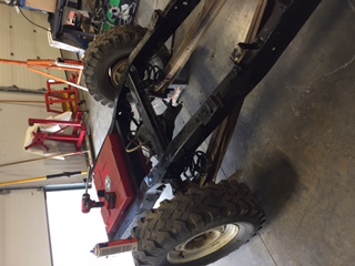 1984 Ford Bronco - The chassis and suspension of a vintage off-road vehicle, possibly a Ford Bronco, is shown in a garage setting. A red fuel tank is mounted…