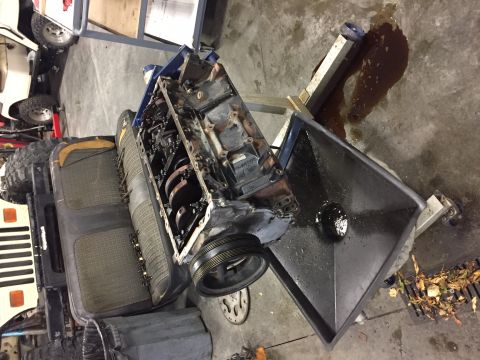 1984 Ford Bronco - An engine block is being drained into a large black funnel on a stand. The engine is partially disassembled and appears to be from an older…
