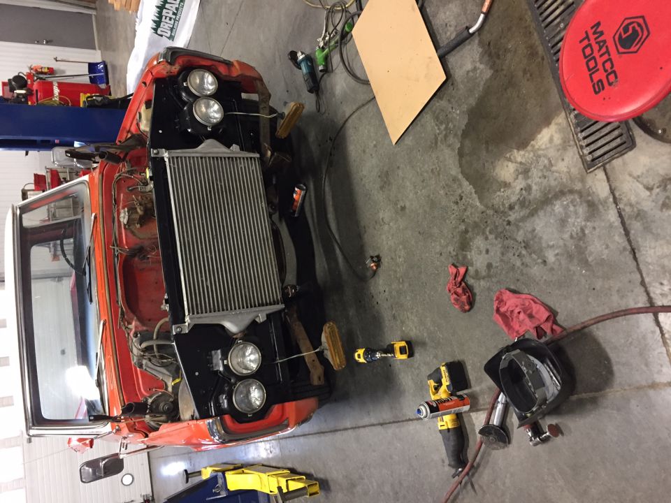 Orange vehicle in garage with hood open, radiator visible, tools on floor.