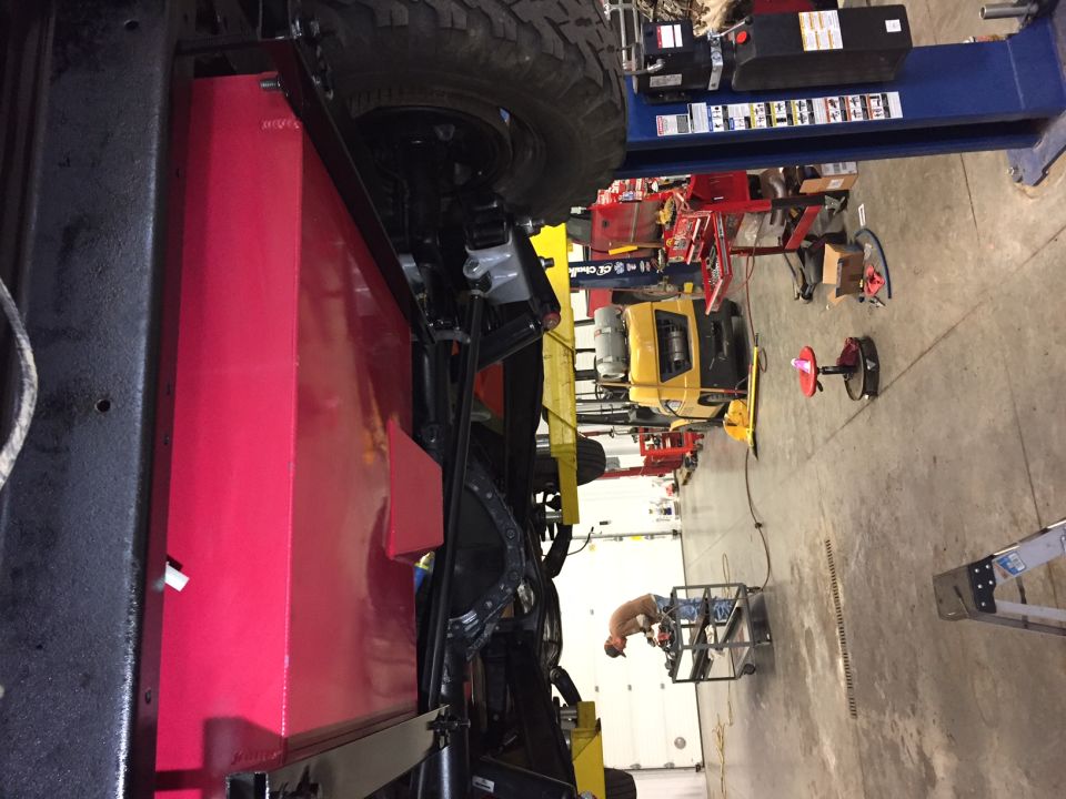Underside of a vehicle on a lift showing a large red fuel tank.