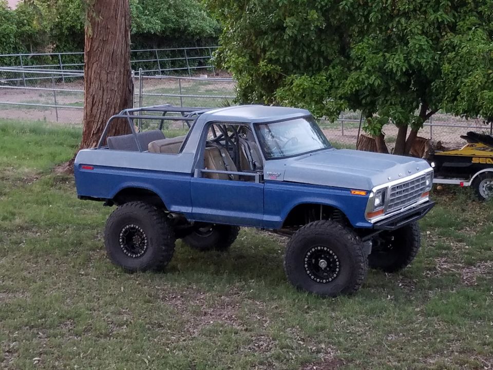Modified blue and gray 1979 Ford Bronco with roll cage and large tires, parked outdoors.