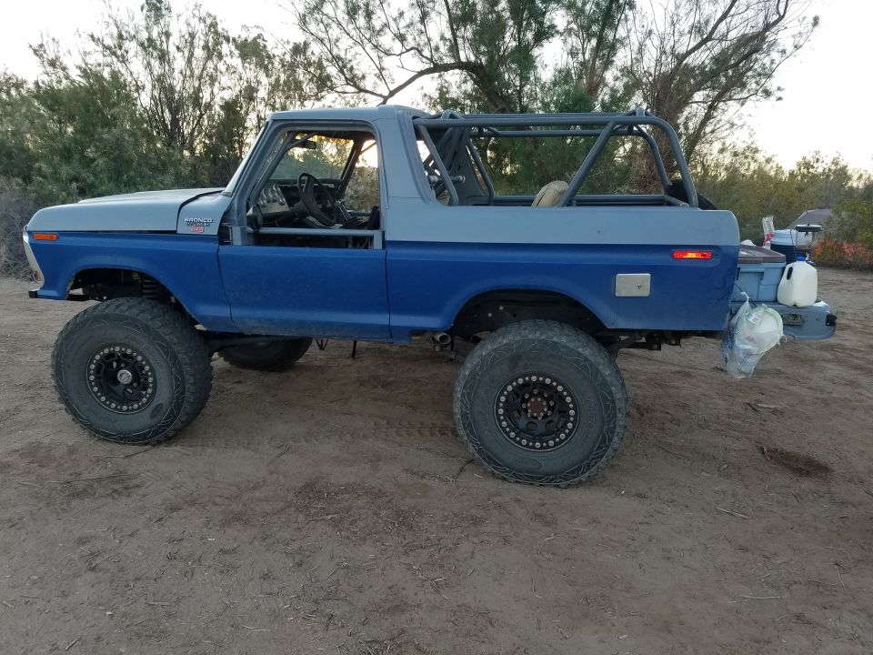 Lifted 1979 Ford Bronco, blue and gray, with roll cage and off-road tires.