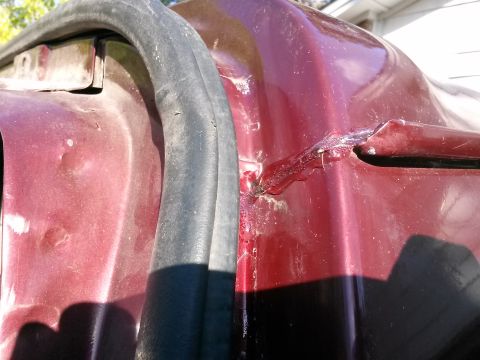 1996 Ford Bronco - Close-up view of the damaged driver's side door jamb area of a dark red vehicle. The metal is dented and appears to have been repaired with…