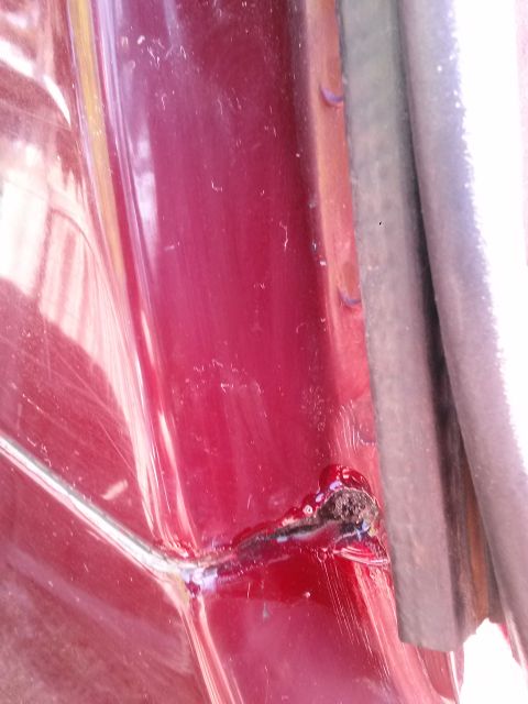 1996 Ford Bronco - A close-up view shows rust and damage on the red painted body of a vehicle, near a rubber seal.