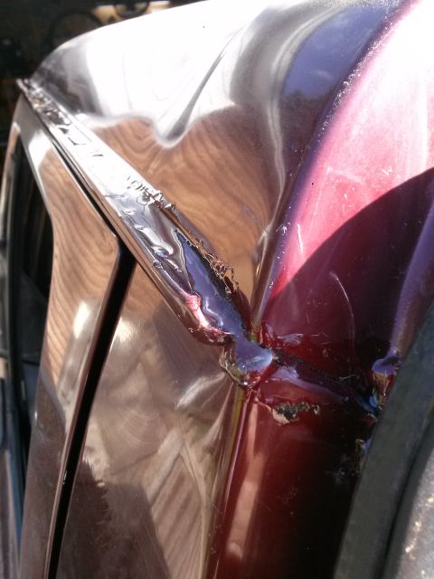 1996 Ford Bronco - A close-up view shows damage to the maroon paint and metal on the edge of a vehicle's body panel. The damaged area reveals exposed metal an…