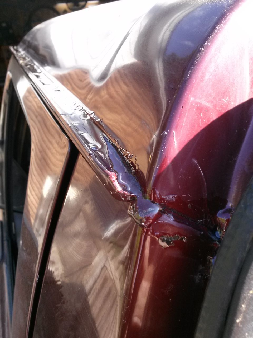 Close-up of damaged maroon car body panel with exposed metal