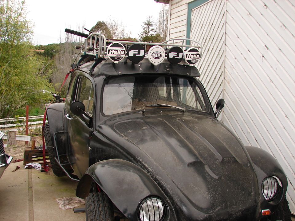 Black modified Volkswagen Beetle with Hella spotlights on roof rack, parked outdoors.