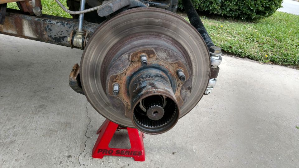 close-up of a vehicle's rusty brake rotor and hub assembly supported by a red jack stand