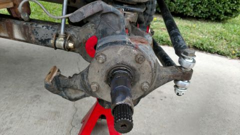 1992 Ford Bronco - Close-up of a vehicle's spindle assembly, supported by a red jack stand, with visible suspension and steering components.