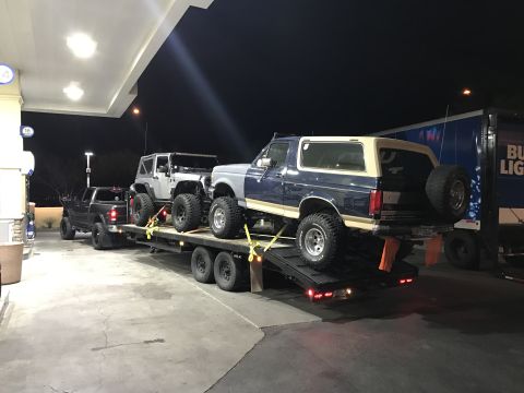1991 Ford Bronco - A blue and tan 1991 Ford Bronco is transported on a trailer alongside other vehicles.