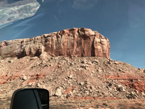 1991 Ford Bronco - View from a vehicle's side mirror shows a large, layered rock formation under a clear blue sky.