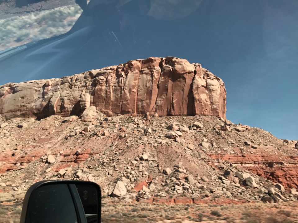 Side mirror reflects a cliff face under a blue sky