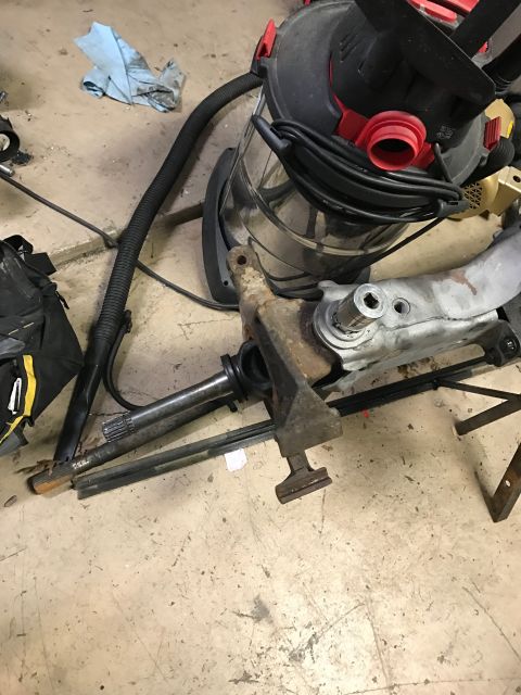 1996 Ford Bronco - A disassembled vehicle suspension part rests on a concrete floor next to a shop vacuum cleaner.