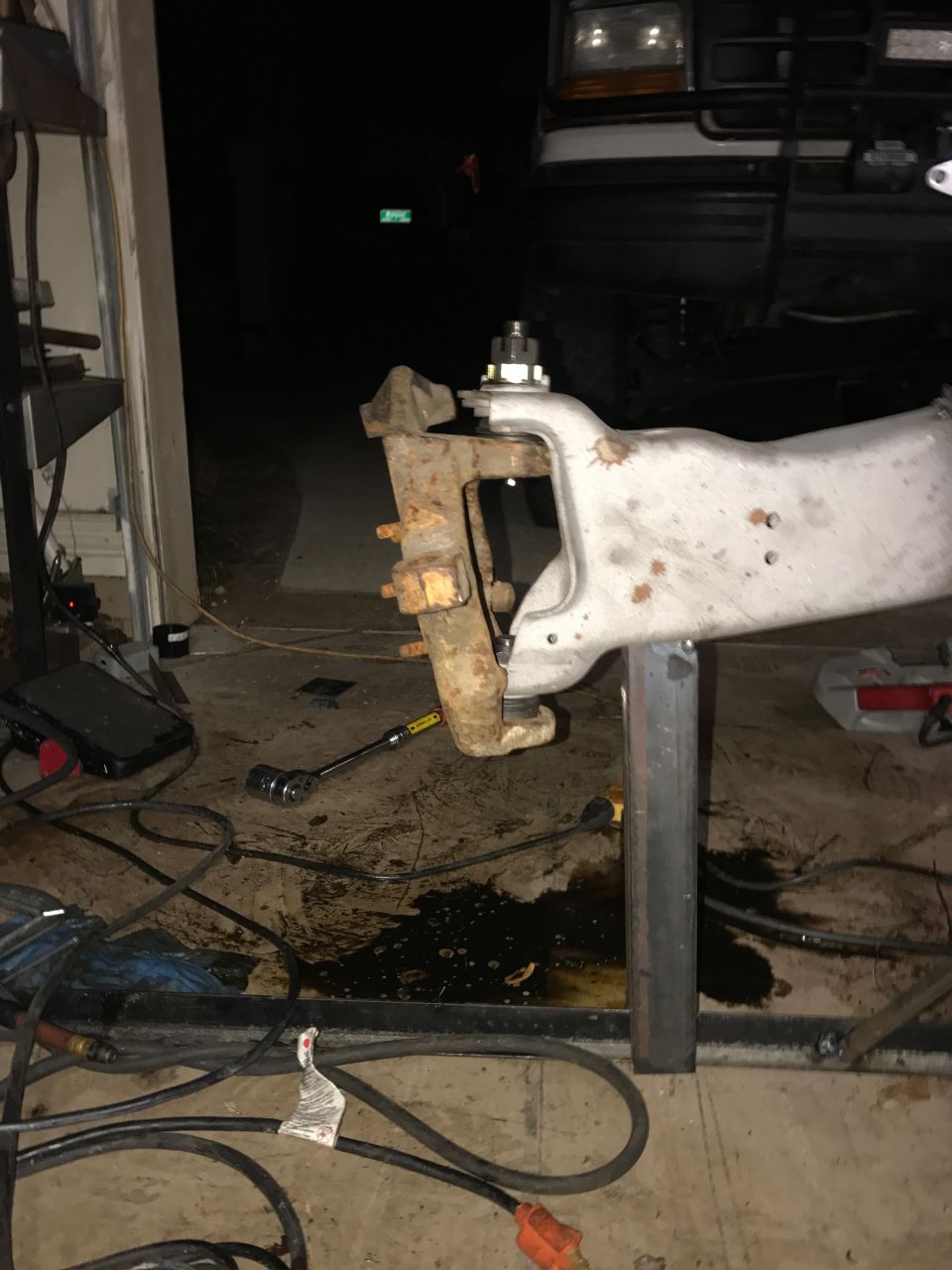Vehicle suspension parts, tools, and oil on garage floor.