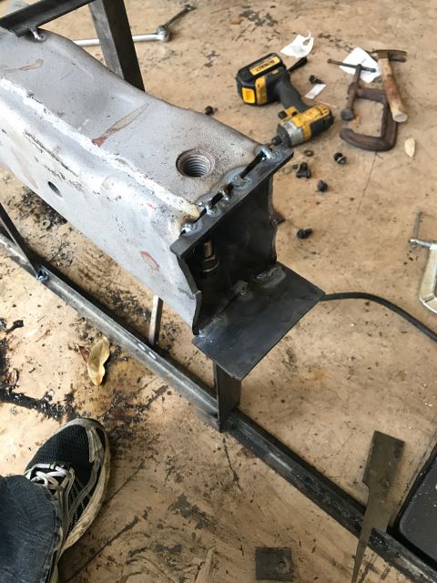 1996 Ford Bronco - A close-up view of a metal beam with visible welding work and a threaded hole. Tools and hardware are scattered on the concrete floor aroun…