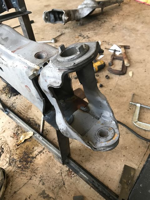 1996 Ford Bronco - A close-up view of a heavily modified or repaired suspension component, possibly a control arm, is shown in a workshop setting. Welds are v…