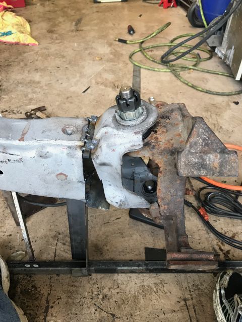 1996 Ford Bronco - A close-up view of a rusty metal component, likely a vehicle suspension part, secured in a vise. The part features a ball joint with a cast…