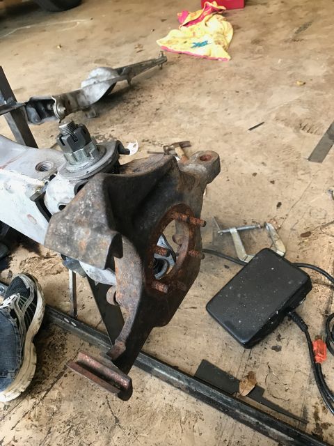 1996 Ford Bronco - A close-up view of a rusty suspension component, likely a spindle or knuckle, with a large nut and bolt assembly. The part is resting on a…