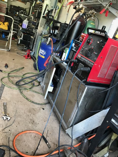 1996 Ford Bronco - A cluttered garage scene with a red Lincoln Square Wave TIG 175 PRO welder in the foreground, along with various tools, hoses, and compress…
