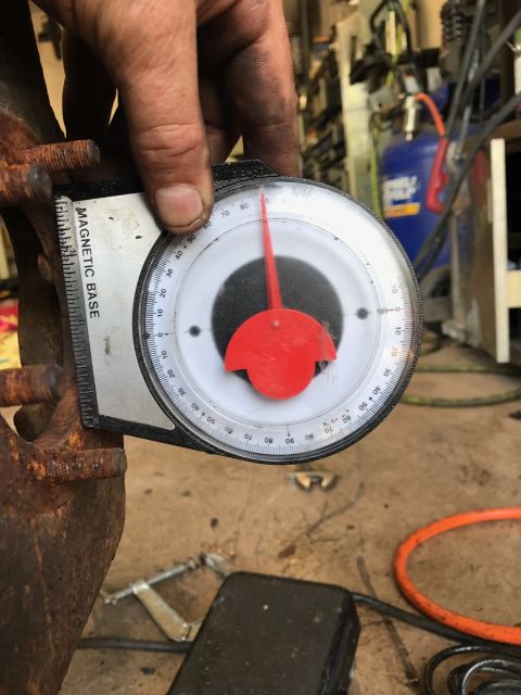 1996 Ford Bronco - A mechanic's hand holds a magnetic base angle finder against a rusty vehicle part, likely a wheel hub, with the gauge showing an angle clos…