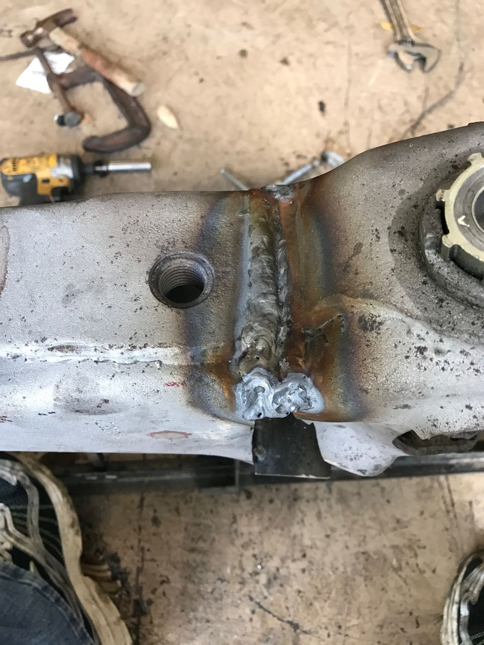 Close-up of a welded metal automotive part with tools and a shoe in the background.
