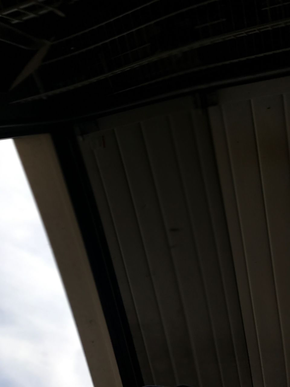 Underside of a dark roof structure with sky and ribbed paneling