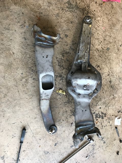 1996 Ford Bronco - Two custom-fabricated metal suspension components are laid out on a concrete floor, showing welds and bolt holes.