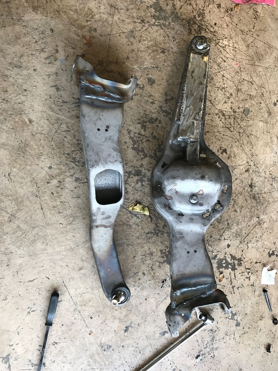 Two custom metal suspension parts with visible welds and bolt holes on a concrete floor.