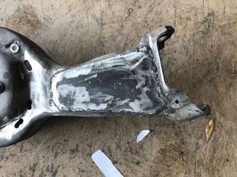 1996 Ford Bronco - A heavily modified metal suspension component, likely a control arm, with extensive welding and grinding visible. The part is resting on a…